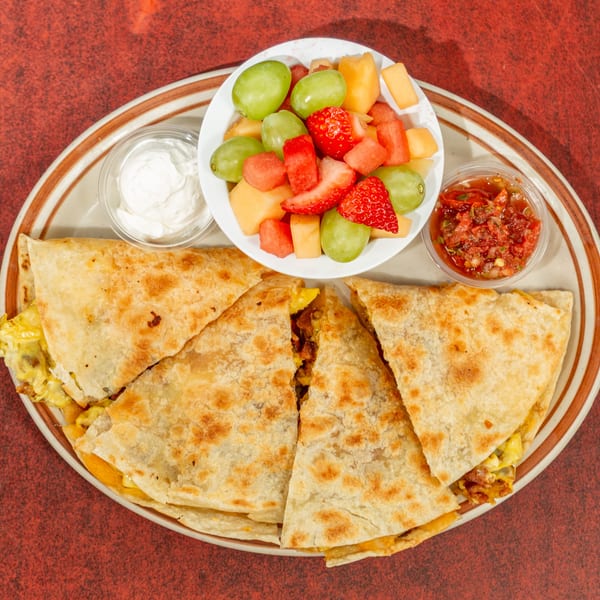 Breakfast quesadillas with scrambled eggs, bacon, fruit salad, sour cream, and salsa.