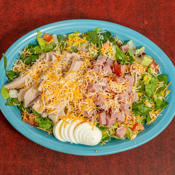 Chef salad with lettuce, tomatoes, cheese, ham, turkey, and sliced hard-boiled eggs on a blue plate.