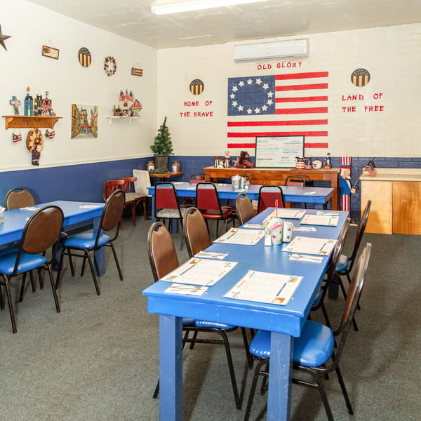 A diner interior with blue tables and chairs, patriotic decor, and a large American flag mural.