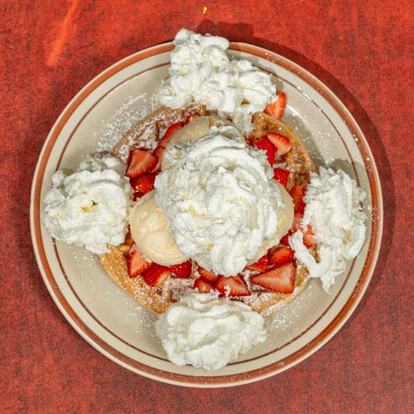 Waffle topped with strawberries, vanilla ice cream, whipped cream, and powdered sugar on a plate.