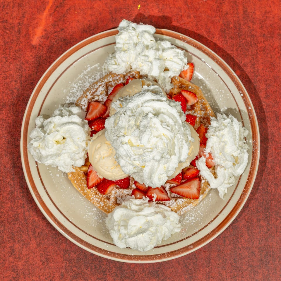 Waffle topped with strawberries, vanilla ice cream, whipped cream, and powdered sugar on a plate.