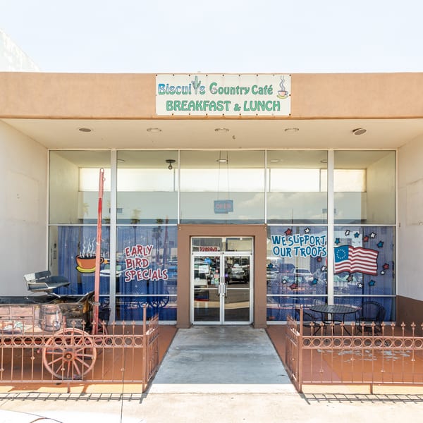 Exterior of Biscuit's Country Café with a wagon, patriotic window decals, and an "OPEN" sign.